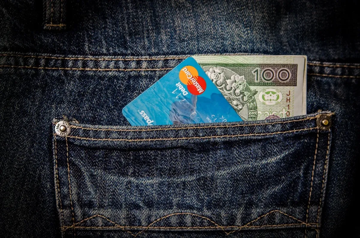 Dłoń wkładająca kartę płatniczą do kieszeni, symbolizująca planowanie budżetu na zakup nowego samochodu.